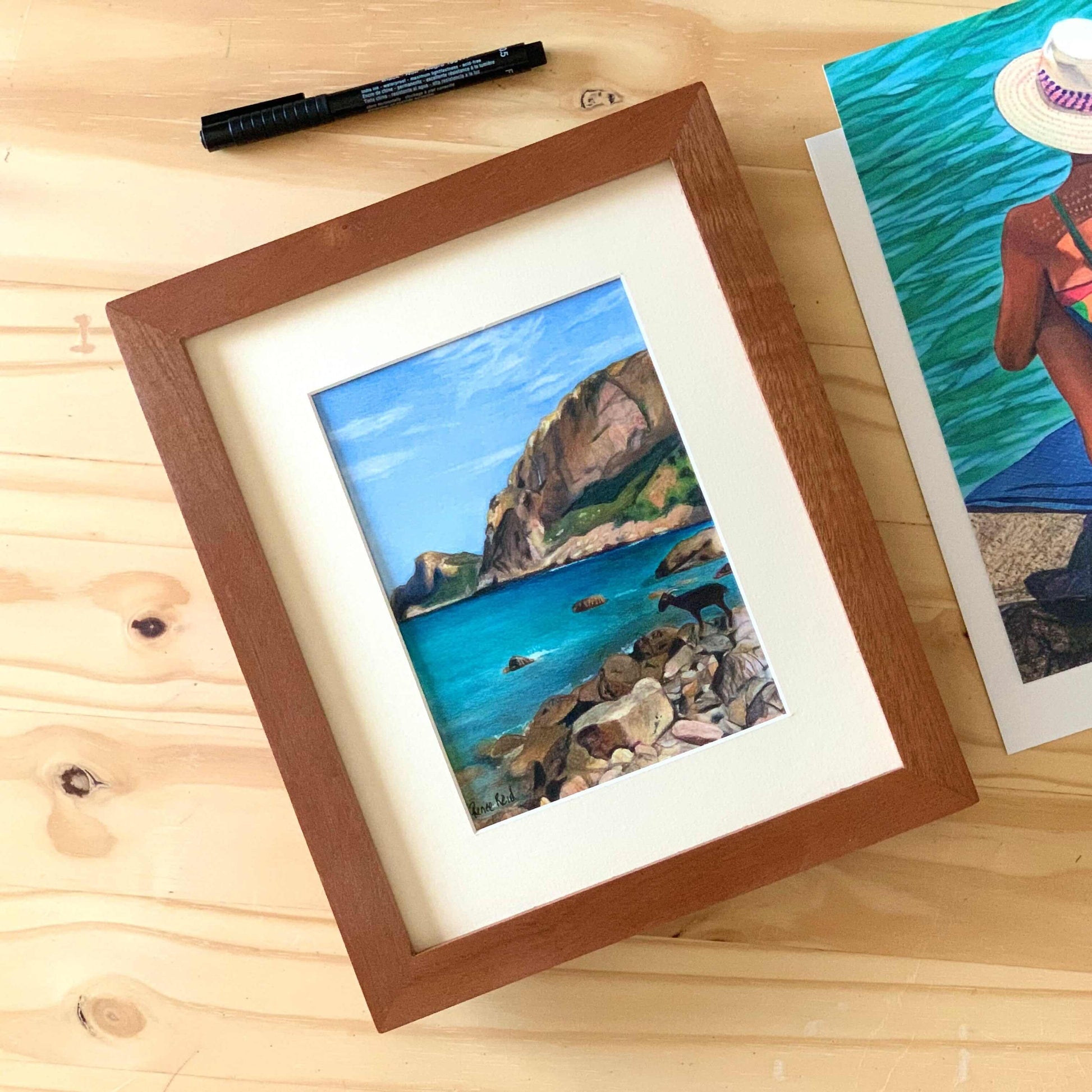 Renee Reid framed original art of a goat on a rocky seaside beach with cliffs in the background