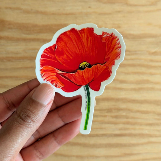 Red Poppy Flower Vinyl Sticker held in hand, featuring vibrant red petals and detailed design.
