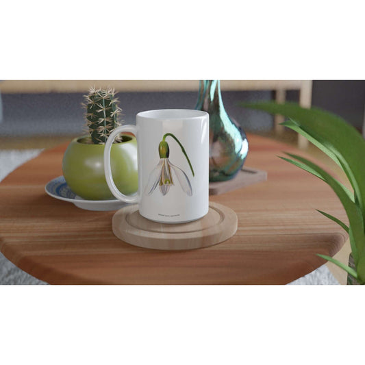 Snowdrop Flower Mug 15oz displayed on a wooden table with a cactus and green vase in the background.