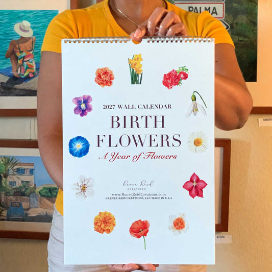 A person holding a 2027 Birth Flower Wall Calendar titled 'BIRTH FLOWERS: A Year of Flowers'  held by artist Renee Reid to show the large vertical calendar size, set against a background of framed art.