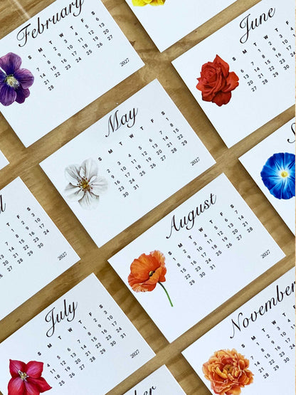A close up view of several montly flower calendars on a wooden table 