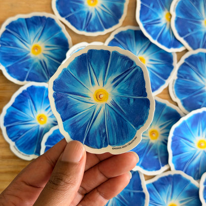 Hand holding a blue flower-shaped sticker with more stickers in the background on a wooden surface.