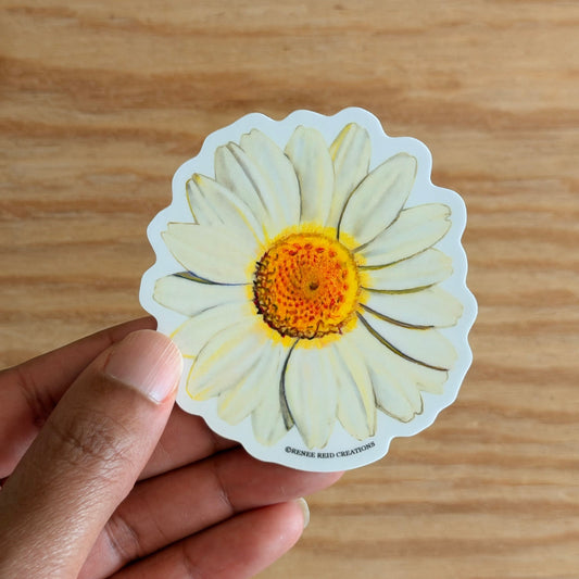 Hand holding a white Daisy Flower Vinyl Sticker on a wooden surface