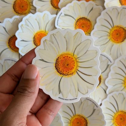 Hand holding a white Daisy Flower Vinyl Stickeragainst a background of similar stickers.