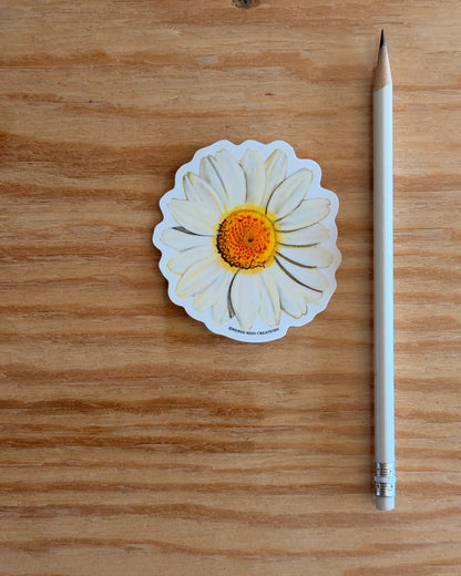 Sticker of a white Daisy Flower Vinyl Sticker on a wooden surface next to a pencil.