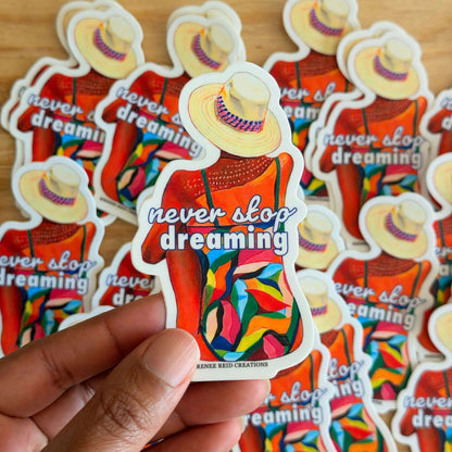 Colorful Dreamers Gaze Vinyl Sticker with 'never stop dreaming' text held by a hand with more stickers on a wooden surface.