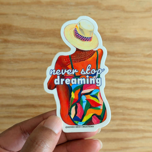 Colorful Dreamers Gaze Vinyl Sticker with 'never stop dreaming' text held by a hand on a wooden surface