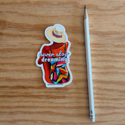 Dreamers Gaze Vinyl Sticker with 'never stop dreaming' text on a wooden surface with a pencil for scale.