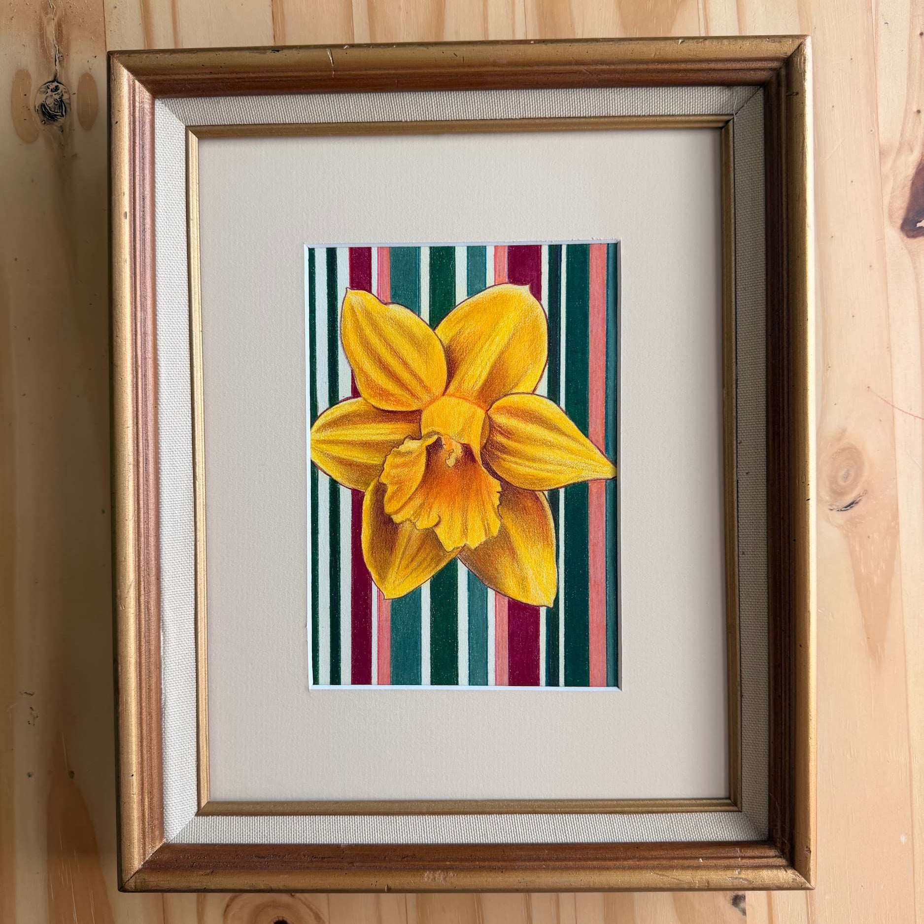 Framed artwork of a yellow flower on a striped background, mounted on a wooden wall.