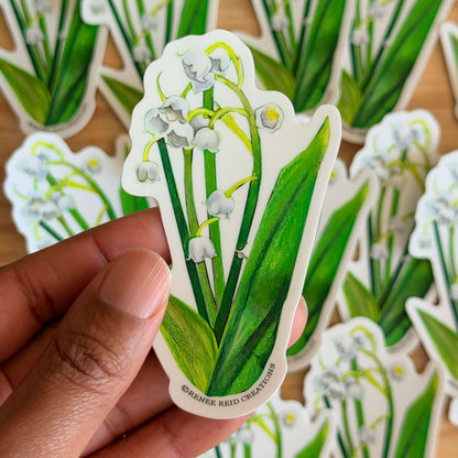 Hand holding a Lily of the Valley Flower Vinyl Sticker on a wooden surface.