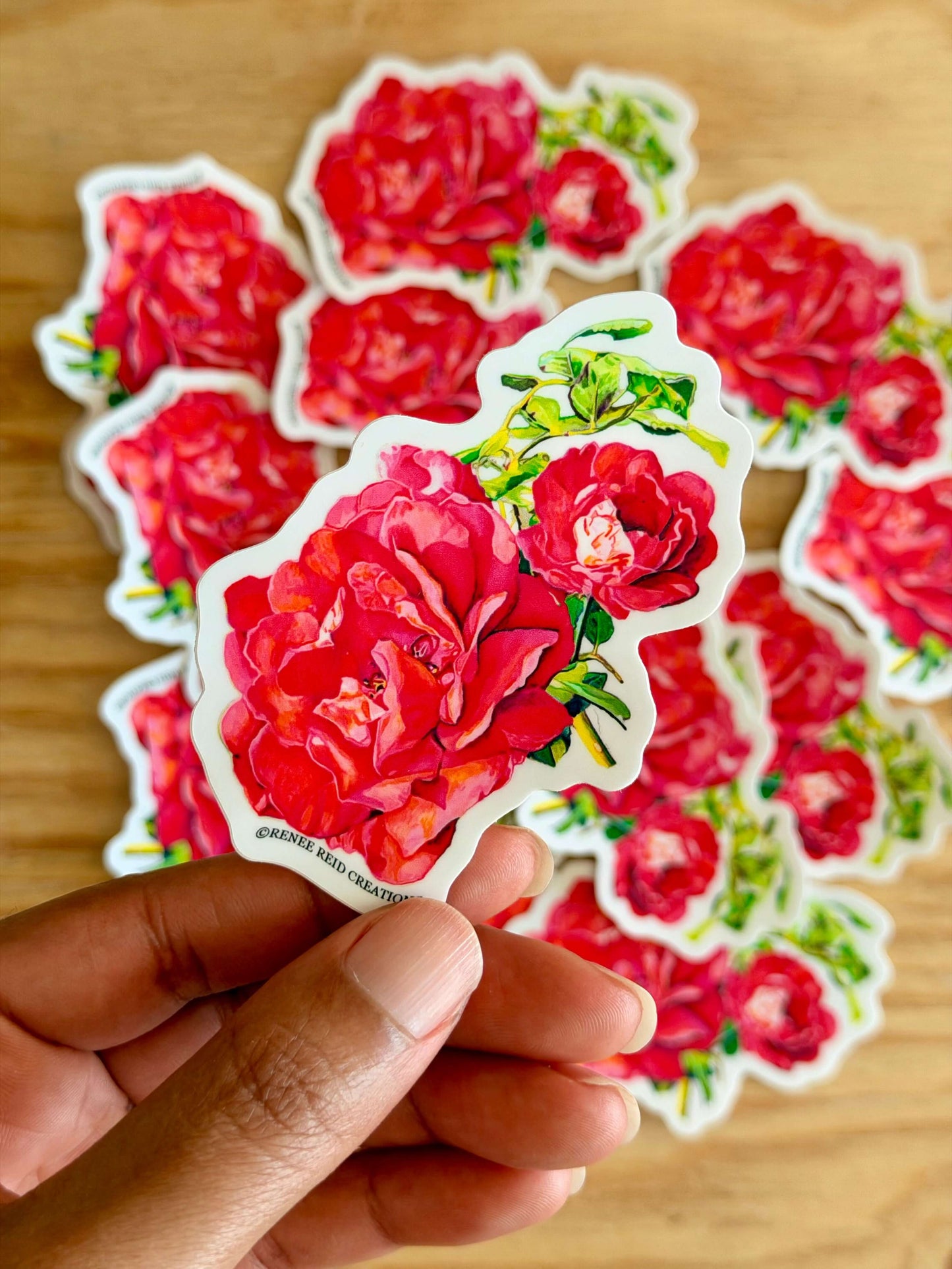 Hand holding a Pink Rose with Leaves Flower with more rose stickers on a wooden surface