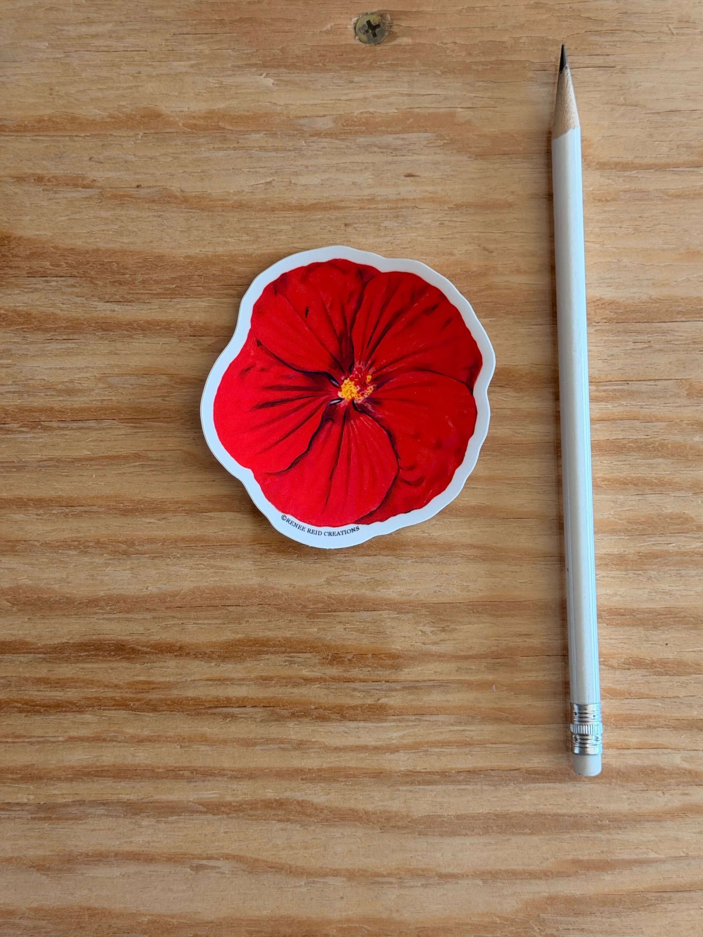 Red Hibiscus Flower Sticker next to a white pencil on a wooden surface