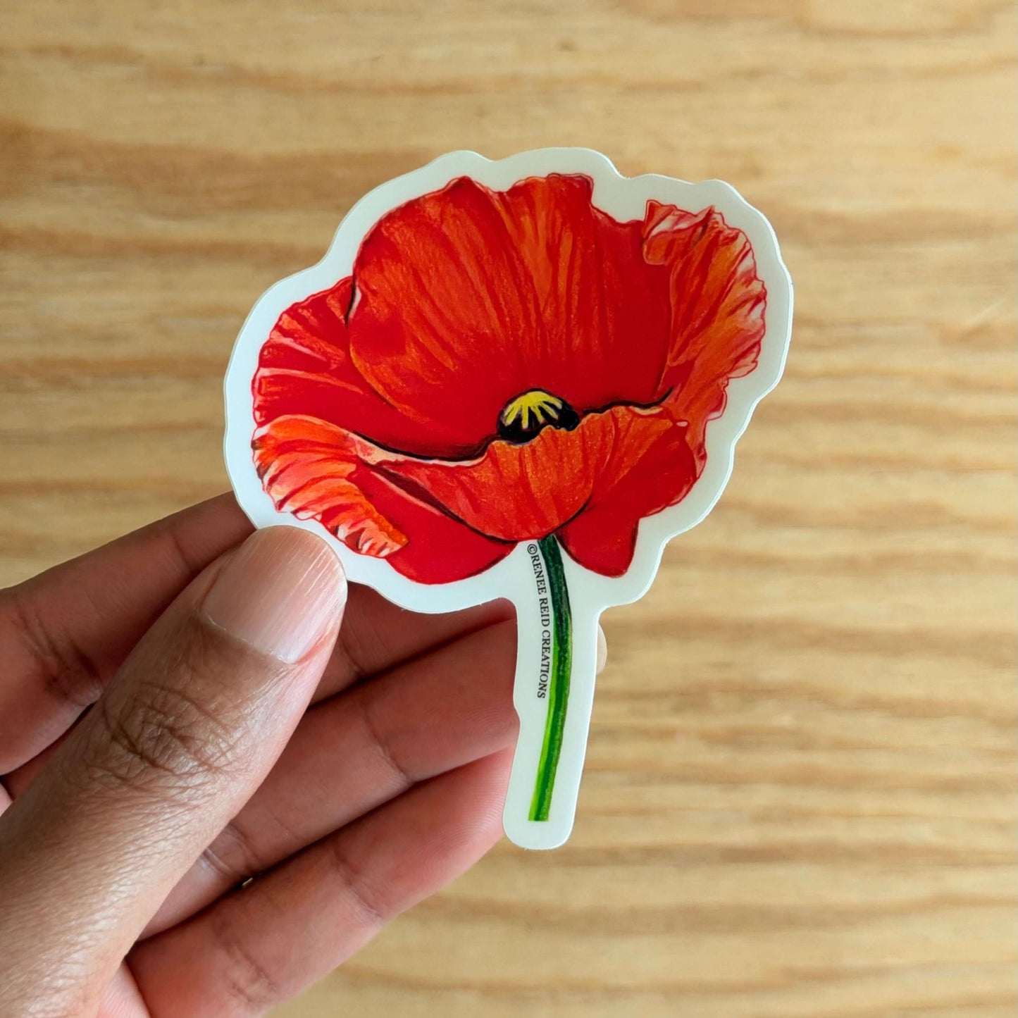 Red Poppy Flower Vinyl Sticker held in hand, featuring vibrant red petals and detailed design.