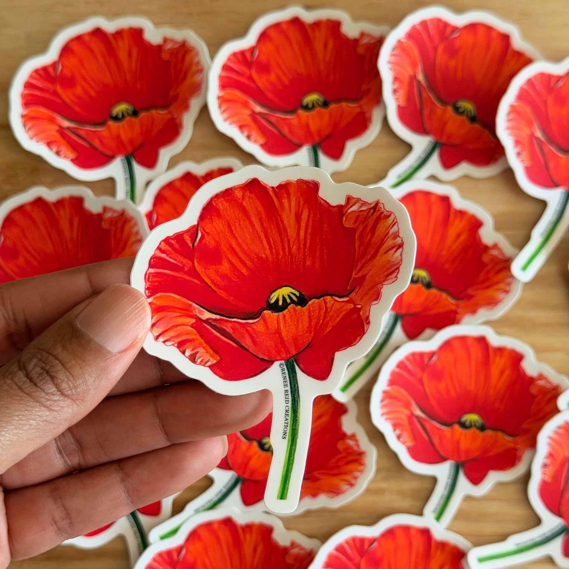 Red Poppy Flower Vinyl Sticker held in hand amongst multiple stickers showcasing vibrant red poppy design.