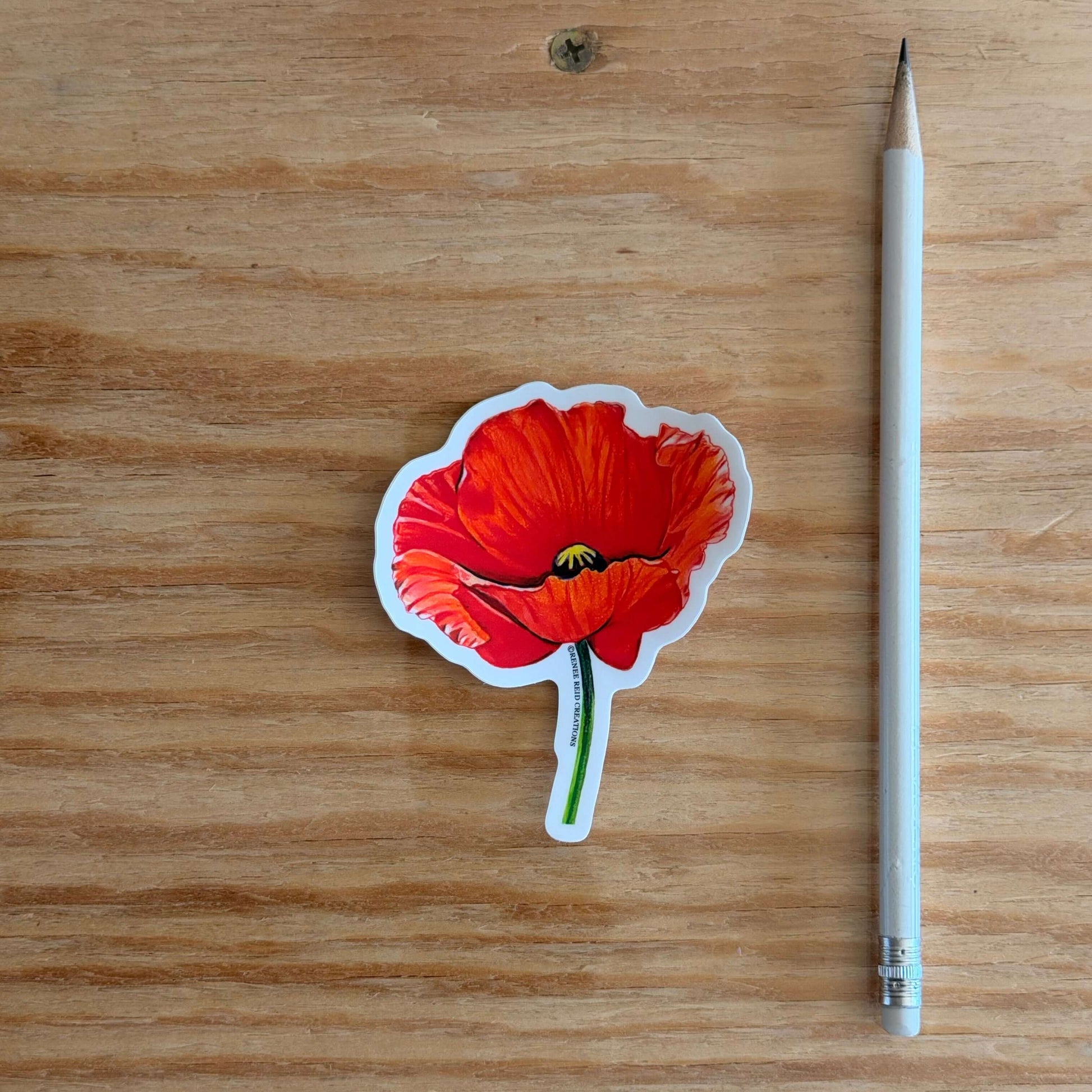 Red Poppy Flower Vinyl Sticker next to a pencil on a wooden surface.
