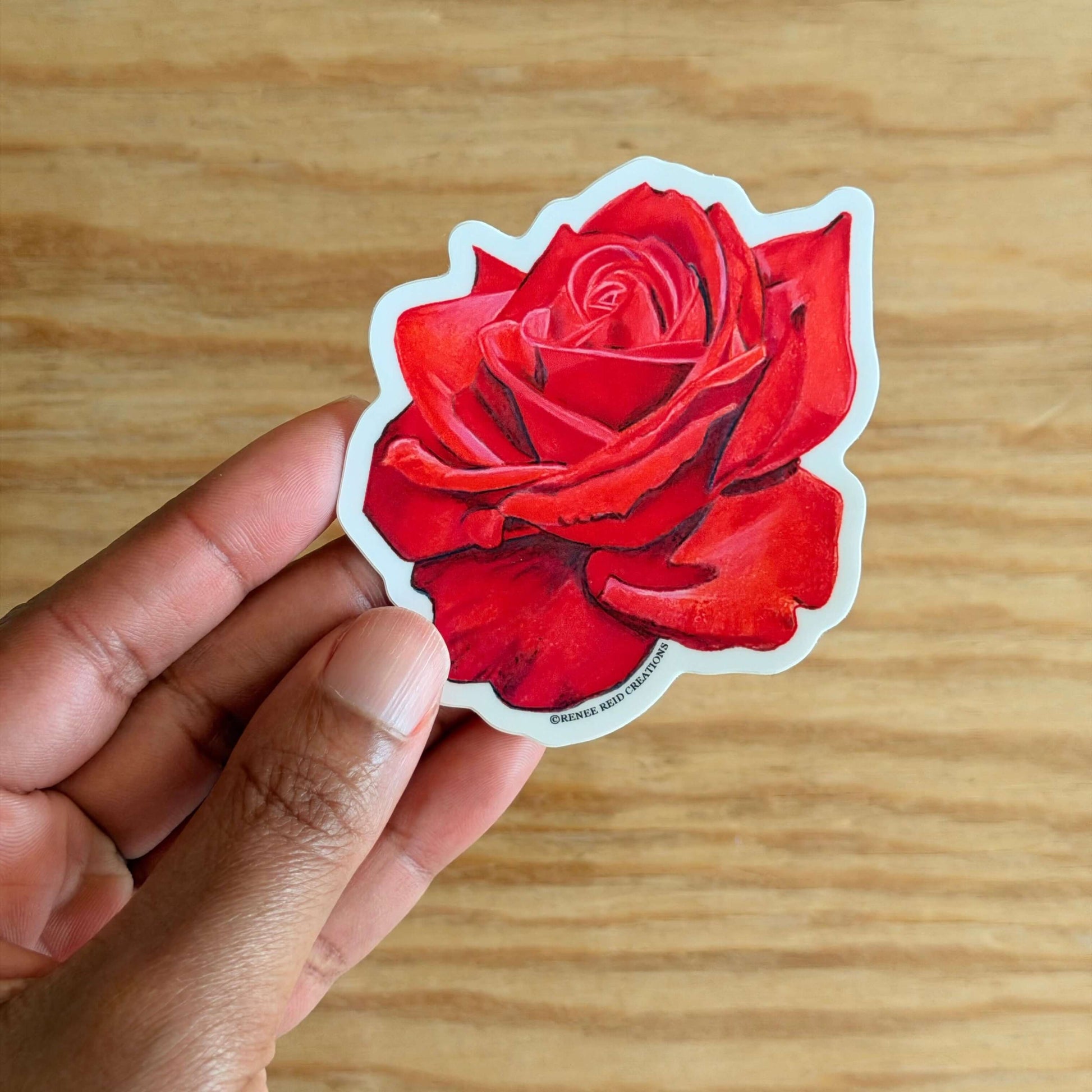Hand holding a Red Rose Flower Vinyl Sticker on a wooden surface
