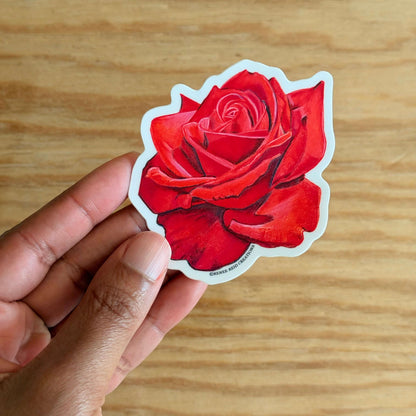 Hand holding a Red Rose Flower Vinyl Sticker on a wooden surface