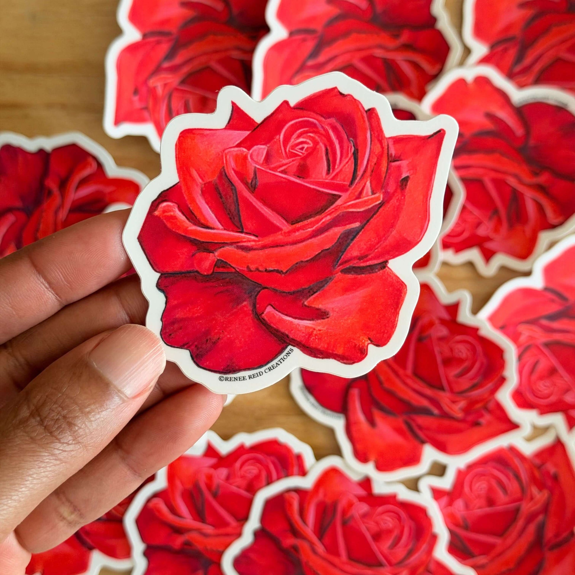 Red Rose Flower Vinyl Stickers on a wooden surface with a hand holding one sticker.