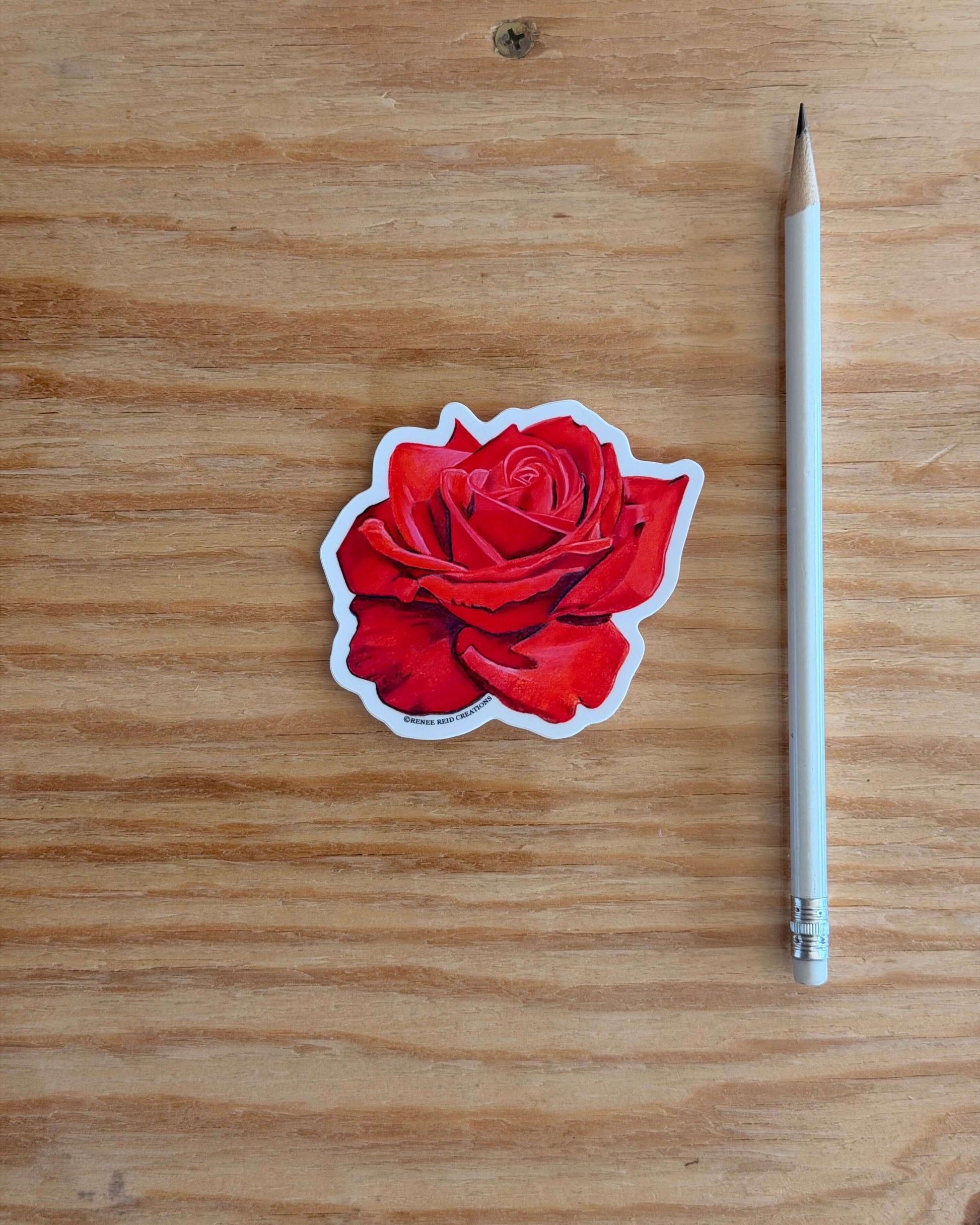 Red Rose Flower Vinyl Sticker and white pencil on a wooden surface